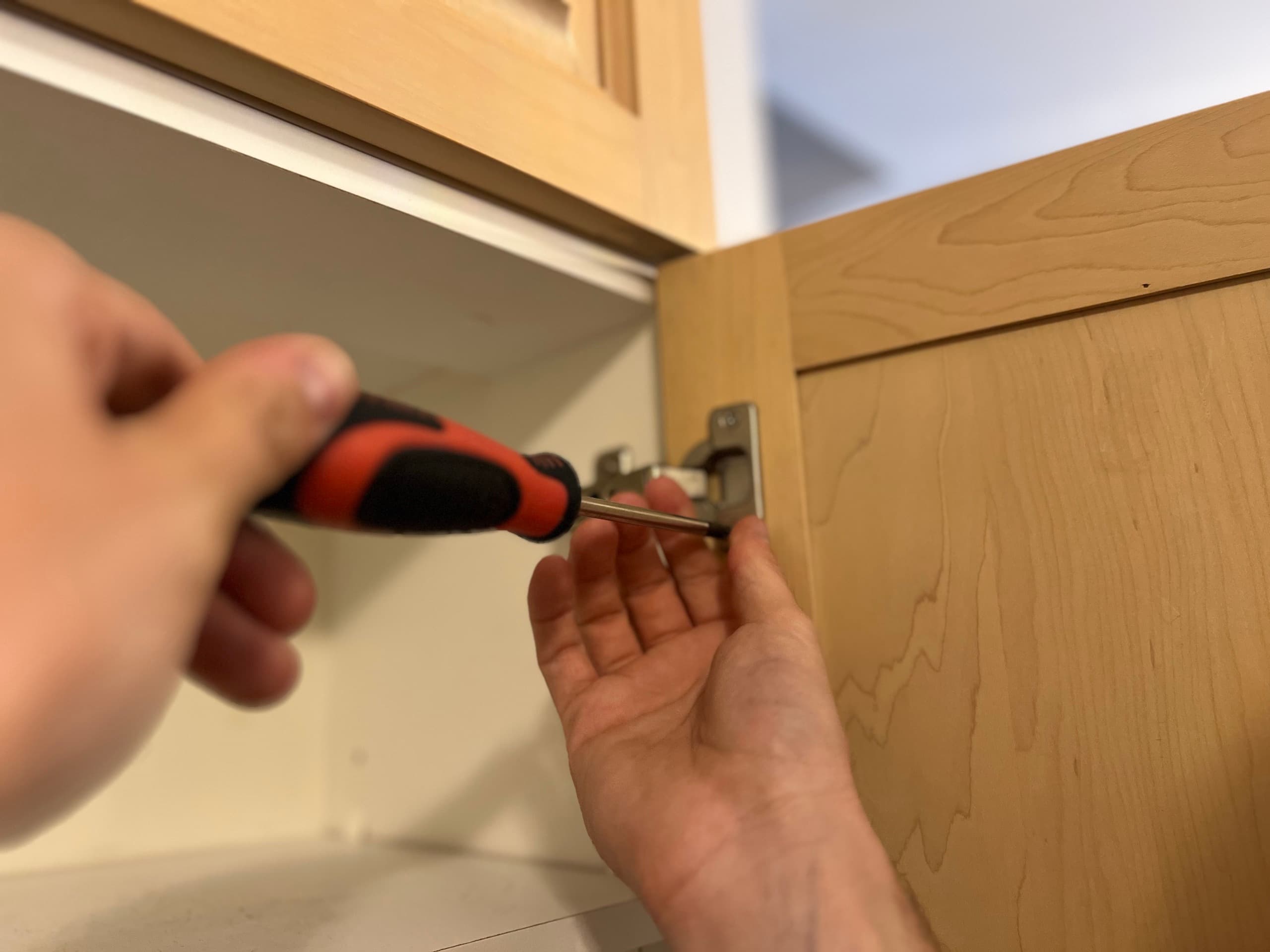 Une charnière dévissée d'une porte d'armoire en érable pendant le démontage